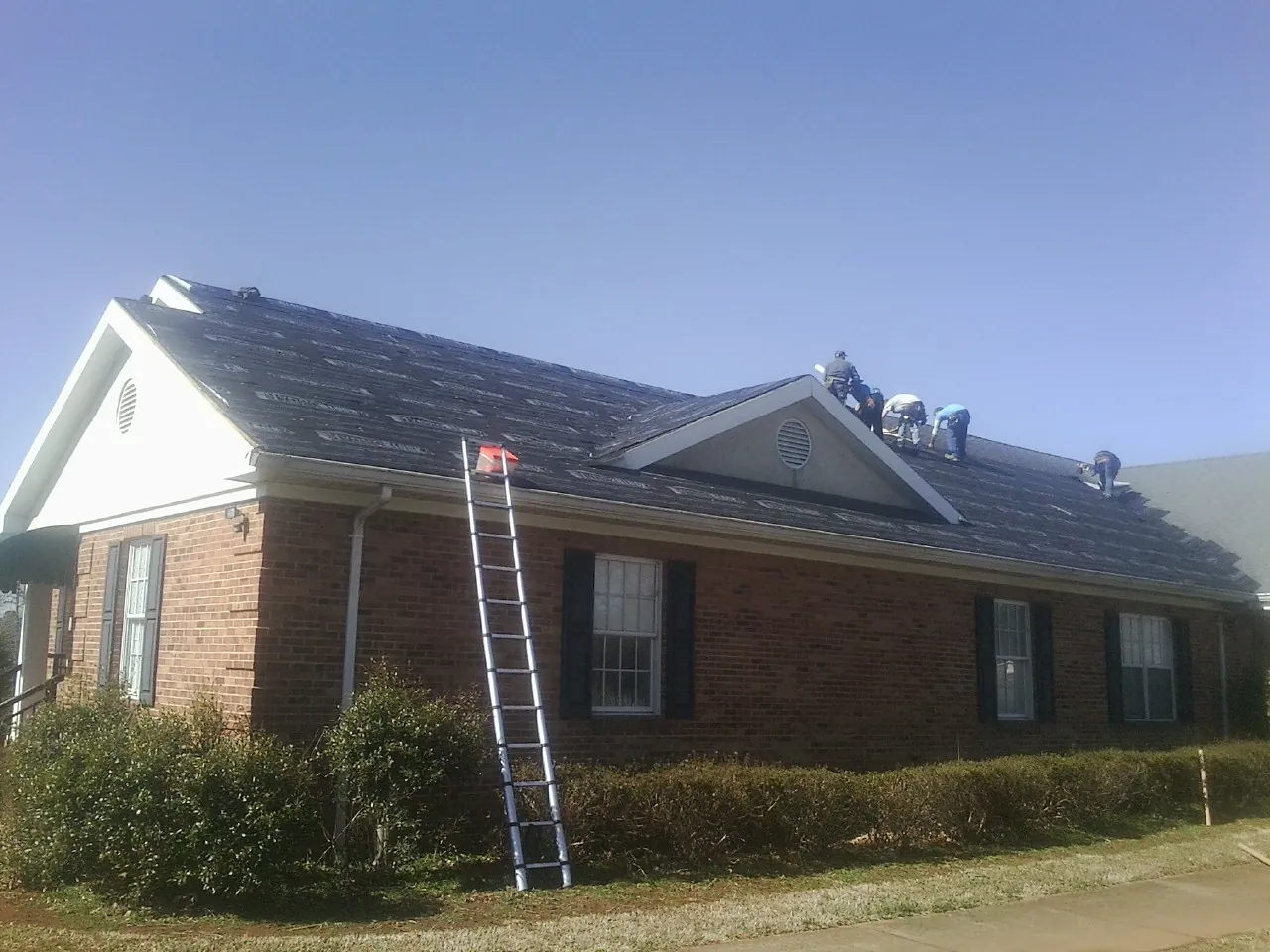 Crew tearing shingles off a brick ranch roof with a ladder set — Metal Roof Repair work by our crew in Escalante