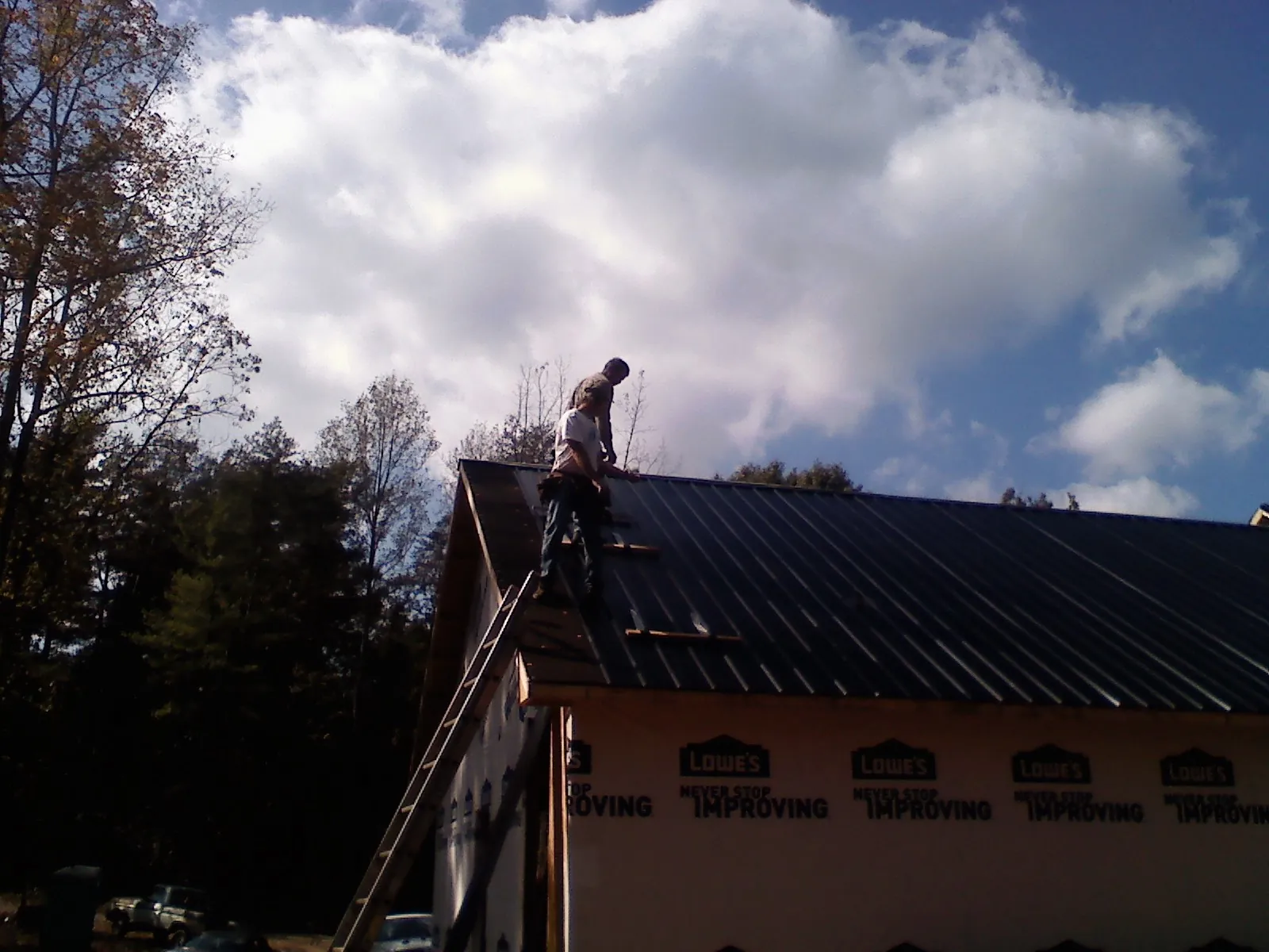 Roofer fastening dark metal panels high against a cloudy sky, from a Roof Inspection job in Escalante